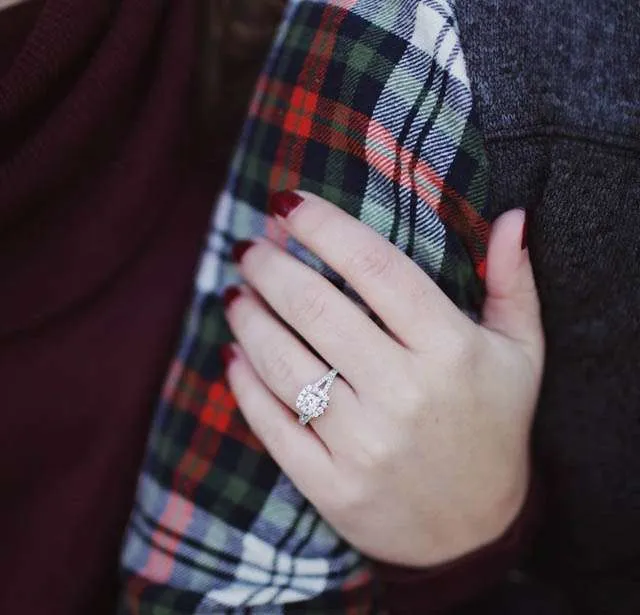 A hand with dark red nail polish rests on a person's arm, showcasing an elegant engagement ring with a large center diamond and smaller surrounding stones, symbolizing commitment and love. The person wears a plaid shirt. This image reflects the importance of nurturing relationships through marriage or couples counseling, fostering communication, understanding, and emotional connection. Rosen Couples Counselling