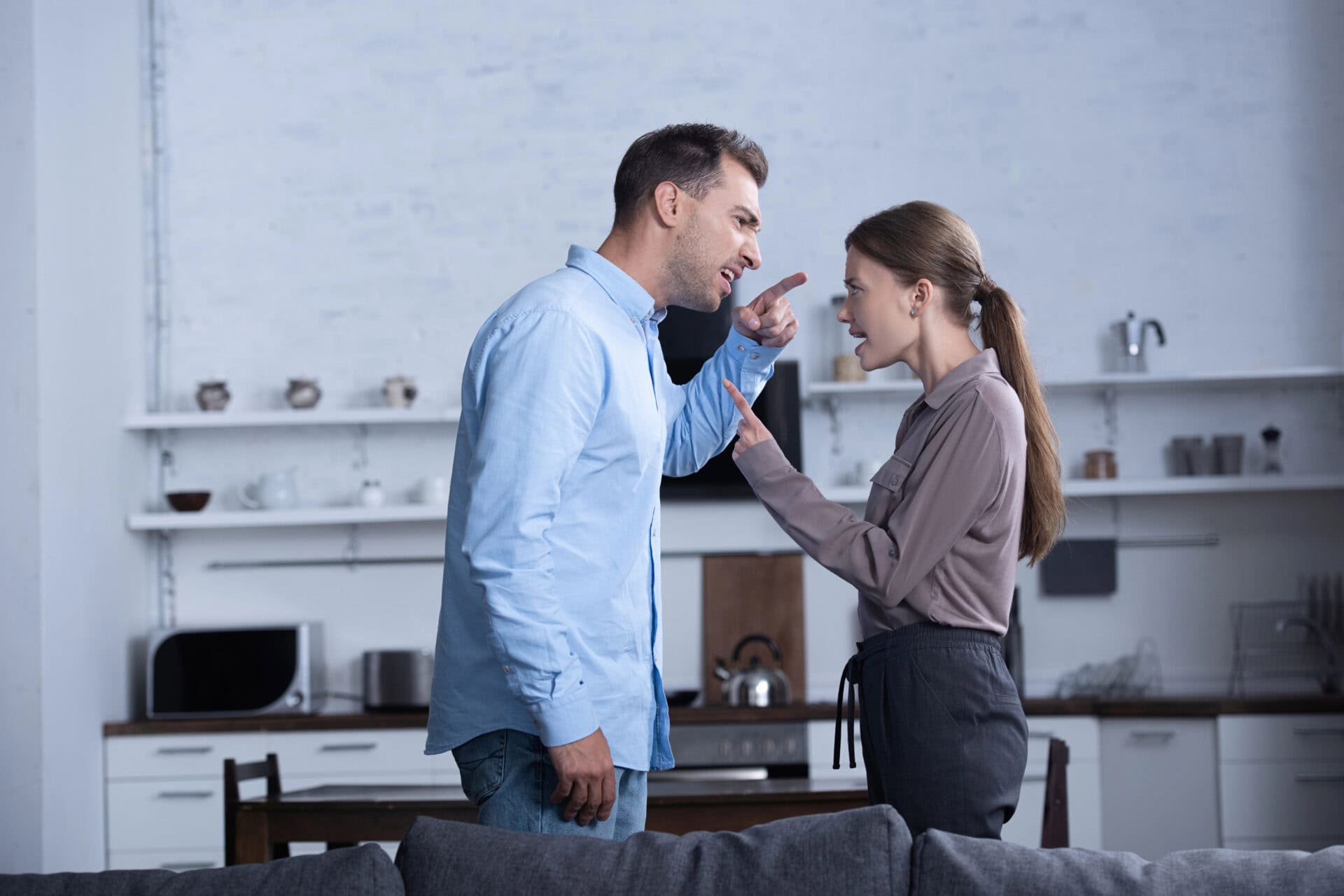 A man and woman are arguing in the kitchen, their voices reflecting a need for anger management and possibly marriage counseling. The man gestures wildly with his hand, while the woman responds with an expressive look, both emotionally engaged in their heated discussion. This tense moment highlights the potential benefits of couples counseling to improve communication and resolve conflicts. Rosen Couples Counselling