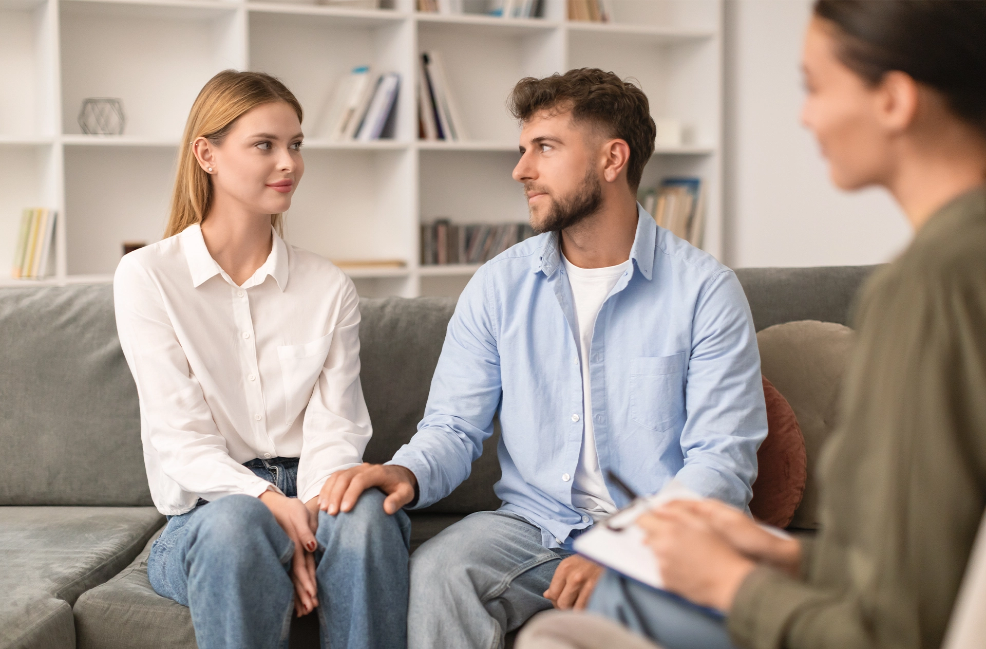 Young couple sitting on sofa together engaging in couples therapy with professional counselor, focusing on reconciliation and finding solutions to strengthen marital bond in psychologist's office